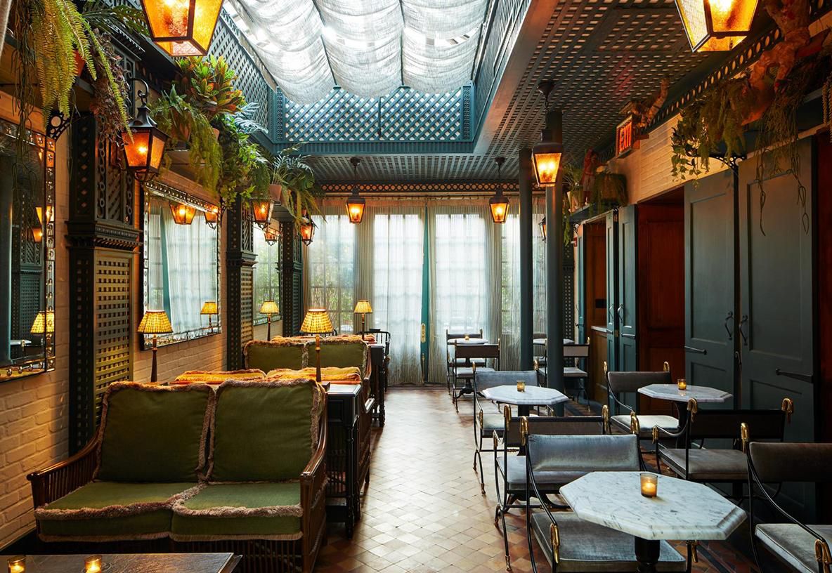 Hotel Chelsea, New York — a long indoor garden room with green velvet seating, hanging lanterns, ferns, and a latticed turquoise ceiling.